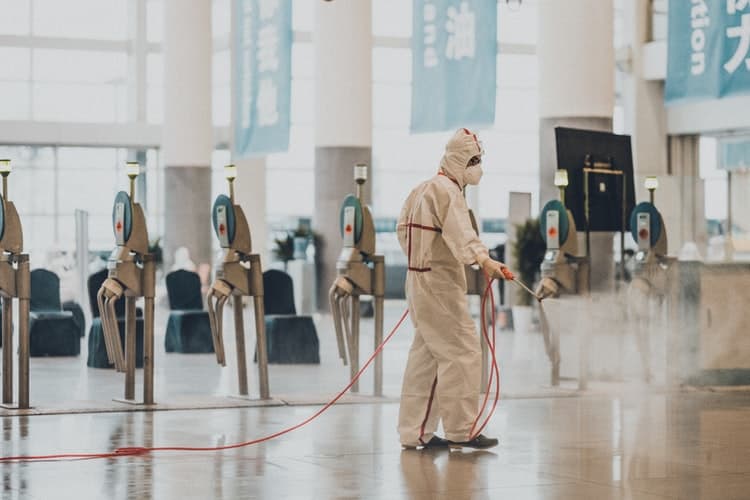 Pessoa em roupa de segurança usa um aparelho de deinfecção no ambiente de um aeroporto